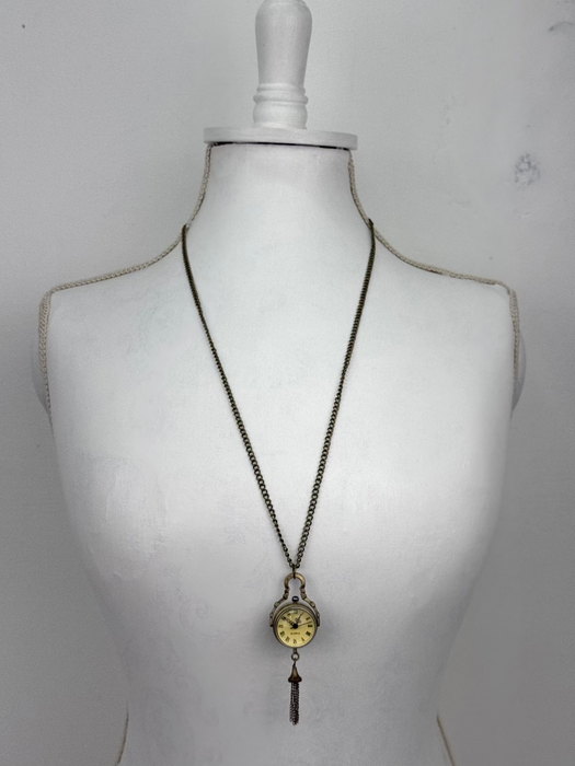Long necklace with a vintage-style pendant on a mannequin bust against a plain background