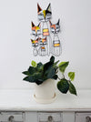 Decorative wall art of cats above a potted plant on a white surface.