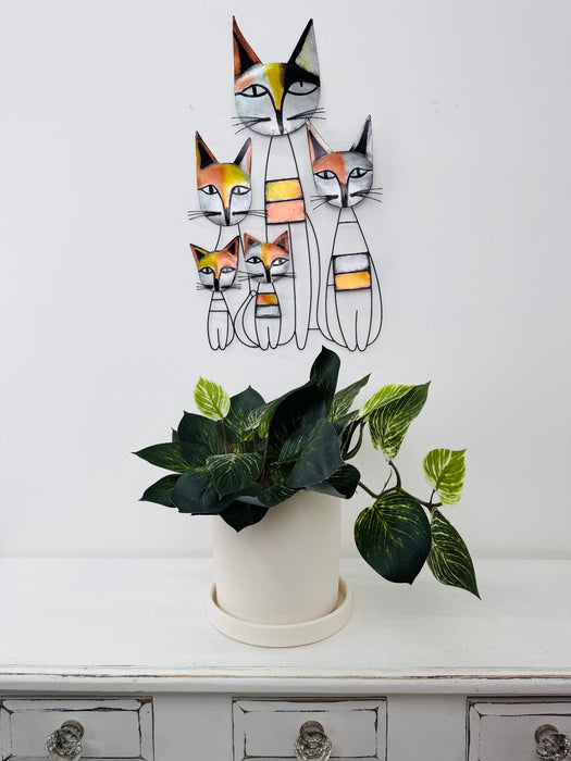 Decorative wall art of cats above a potted plant on a white surface.