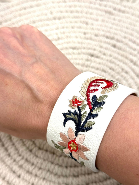 White bracelet with floral embroidery on a wrist against a textured white background