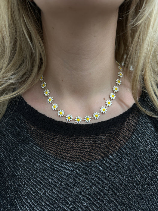 A close-up image of a person wearing a gold-tone chain necklace adorned with daisy flowers.