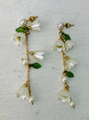 A pair of earrings featuring white lily flowers, green leaves, and gold-colored accents.