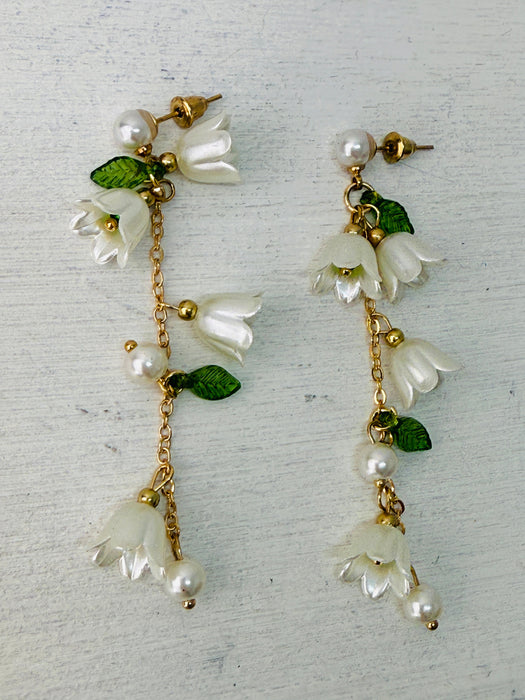 A pair of earrings featuring white lily flowers, green leaves, and gold-colored accents.