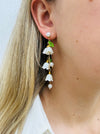 A pair of white flower bell drop earrings with pearl accents and green leaf details.