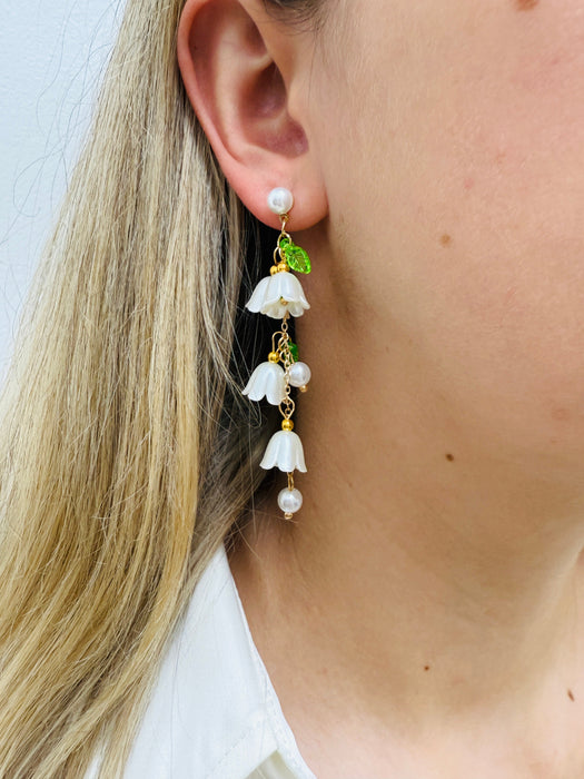 A pair of white flower bell drop earrings with pearl accents and green leaf details.