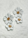 White floral earrings with gold centers on a textured white background