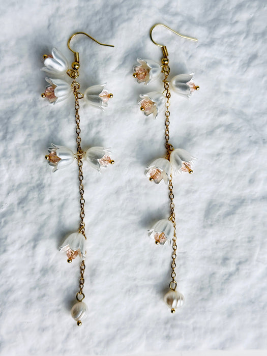 Floral earrings with gold chains on a textured white background