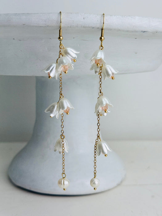 Floral earrings with gold chains on a white stand
