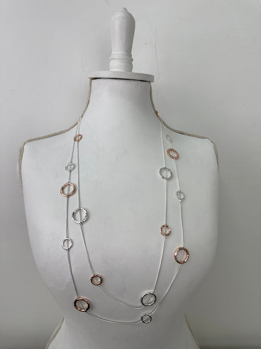long silver and rose gold necklace with textured circle charms displayed on mannequin