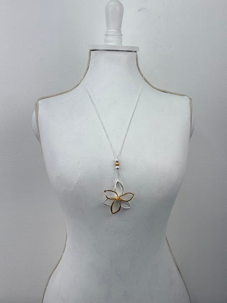 Mannequin wearing a white dress with a gold floral brooch on a light gray background