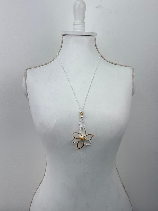 Mannequin wearing a white dress with a gold floral brooch on a light gray background