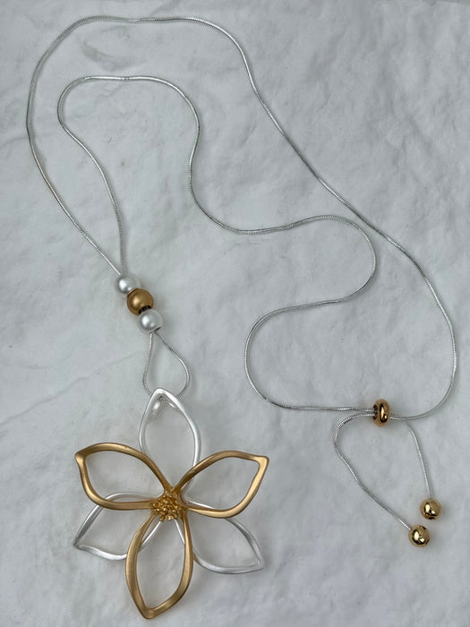 Gold and silver floral pendant on a string against a light gray background