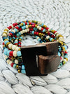 A multicolored beaded bracelet with a hand-carved natural wood buckle, displayed on a woven mat.