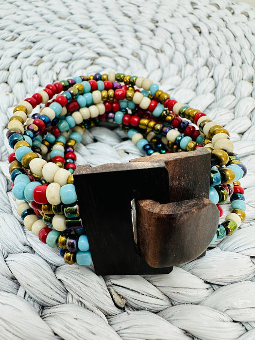 A multicolored beaded bracelet with a hand-carved natural wood buckle, displayed on a woven mat.