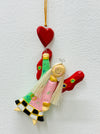 Hand-painted wooden hanging angel with pink dress, green accents and red heart on a gold string.