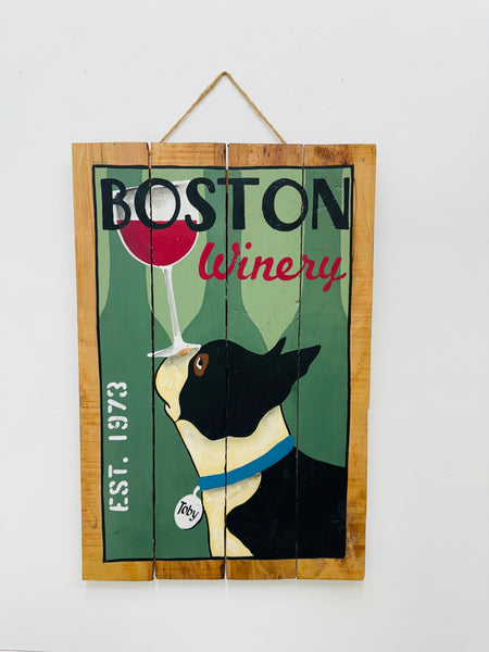 Hand-painted Boston Winery wooden sign with dog and wine glass illustration and hanging rope on white background.