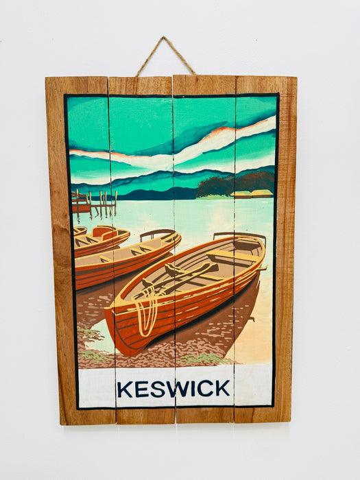 Hand-painted Keswick wooden sign with rowing boats illustration and hanging rope on white background.