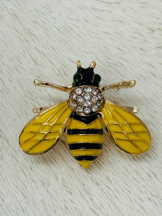 A brooch designed as a honeybee with yellow wings, black and gold accents, and a studded pattern on the body.