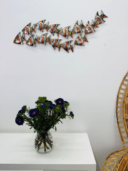 Zebra fish shoal metal wall art displayed above table in coastal interior.