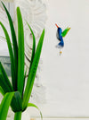 display view of metal humming bird hook next to a green plant