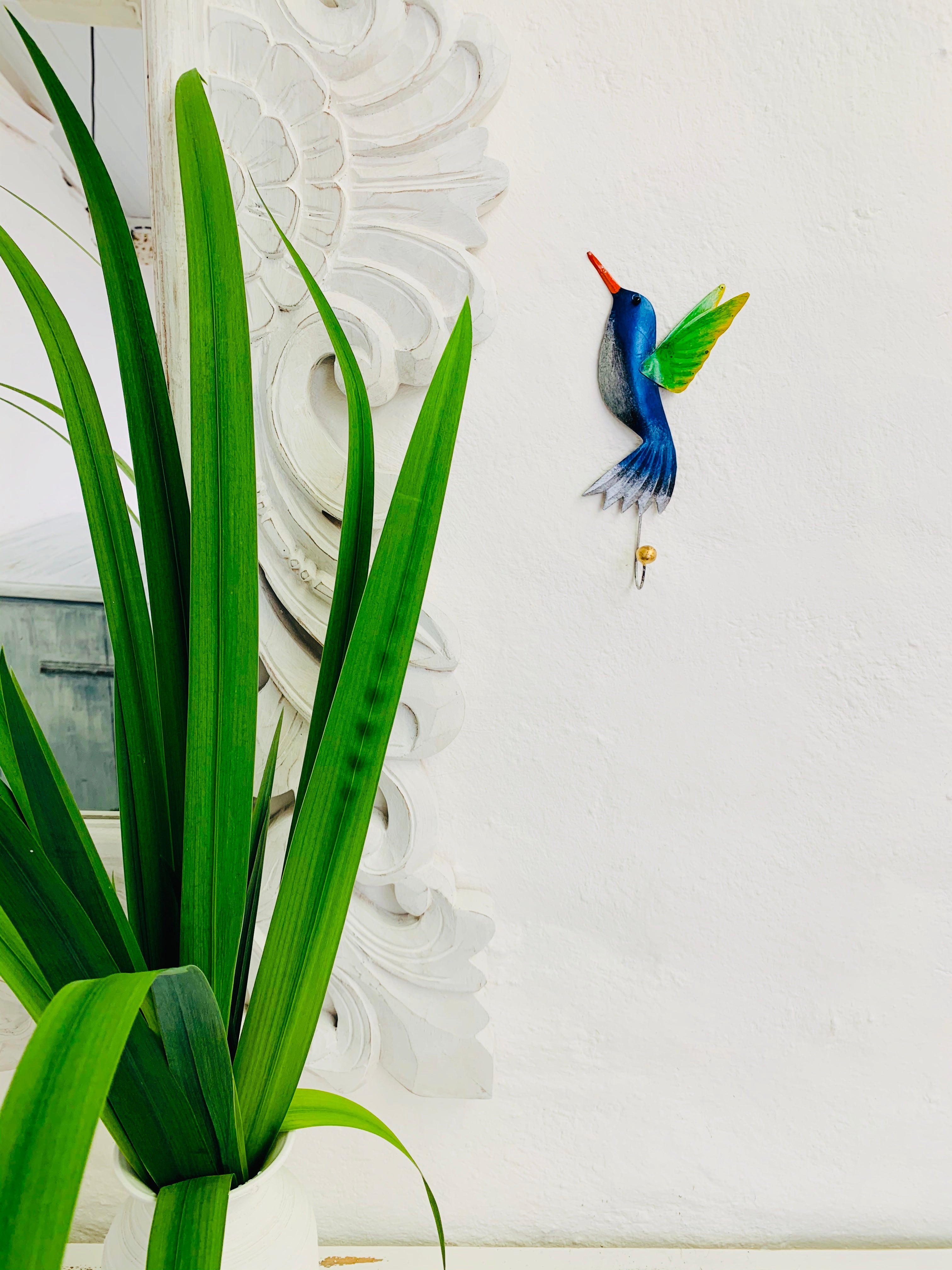 display view of metal humming bird hook next to a green plant