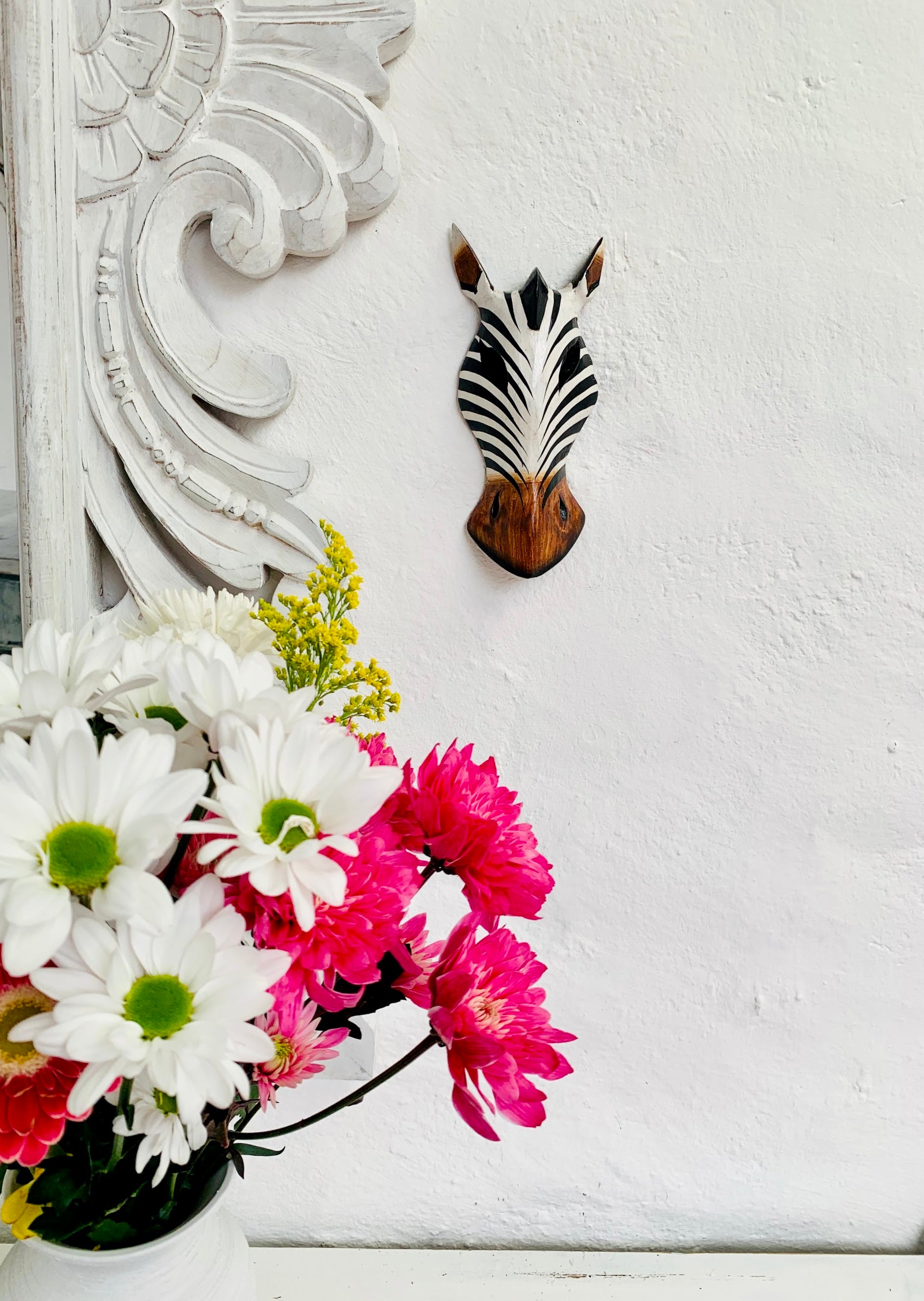 front view of zebra wood mask next to a vase of colourful flowers