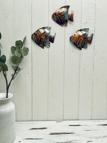 Copper banner fish metal wall art displayed on a white panel wall with decorative plant