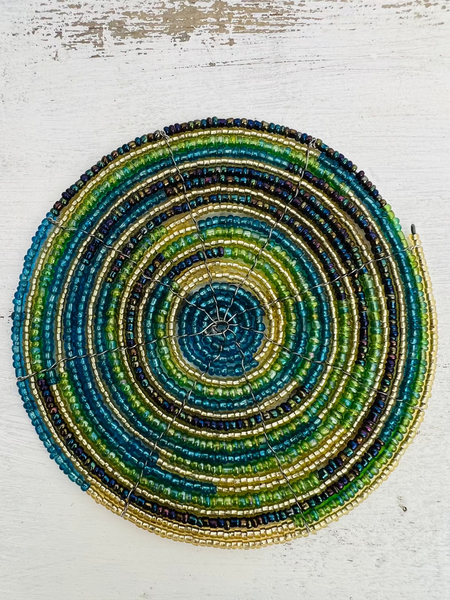 A round beaded coaster with a spiral pattern in multiple colors, including gold, blue, and green, displayed on a white background.