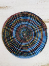 A round, handmade beaded coaster featuring a spiral pattern with colors including blue, gold, and other shades