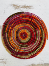 A round beaded coaster with orange, red and gold colors, displayed on a white surface.