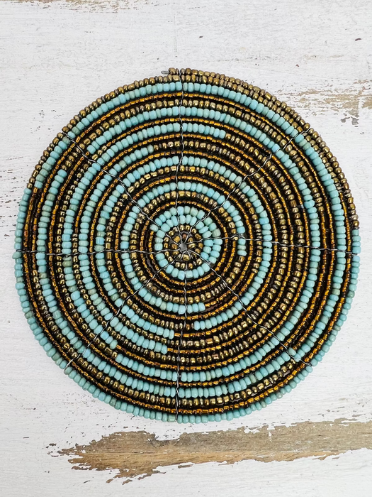 A circular beaded coaster with a turquoise and gold color pattern, placed on a wooden surface.