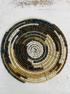 A round beaded coaster with a geometric pattern in white, gold, and paua (abalone) colors.