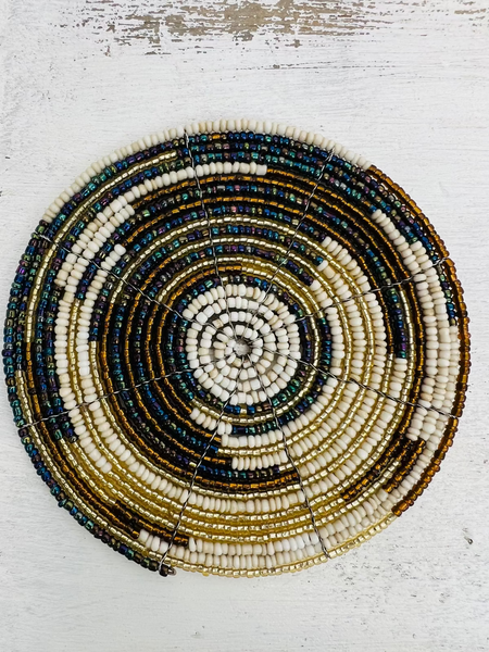 A round beaded coaster with a geometric pattern in white, gold, and paua (abalone) colors.