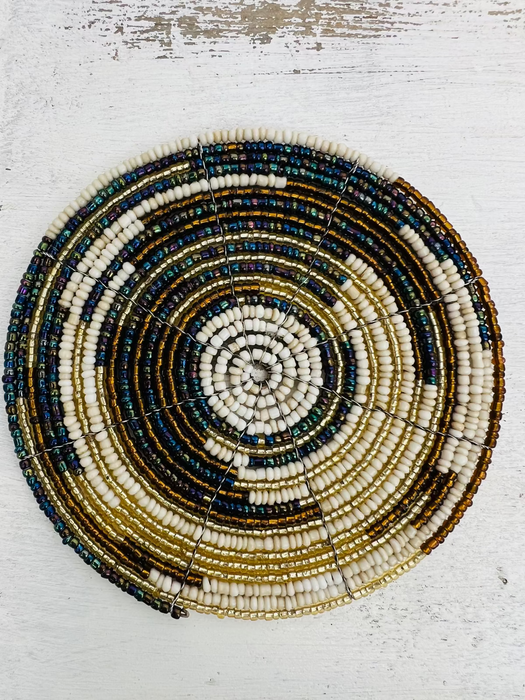 A round beaded coaster with a geometric pattern in white, gold, and paua (abalone) colors.