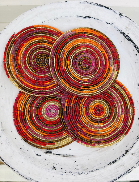 Set of orange, red and gold beaded coasters arranged together on a light wooden background.