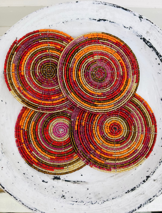 Set of orange, red and gold beaded coasters arranged together on a light wooden background.