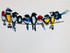 Close-up of hand-painted metal birds on a wire showing colourful feathers and golden details