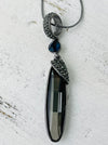 A long silver necklace with an elegant Art Deco style pendant, featuring gunmetal grey plating and a blue accent.