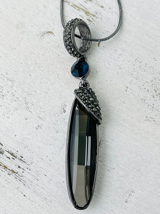 A long silver necklace with an elegant Art Deco style pendant, featuring gunmetal grey plating and a blue accent.