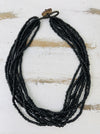 A multi-strand black beaded necklace with a dark metal clasp, displayed on a distressed white wooden surface.