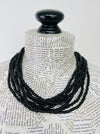 A black beaded necklace displayed on a book-print mannequin bust against a plain white background.