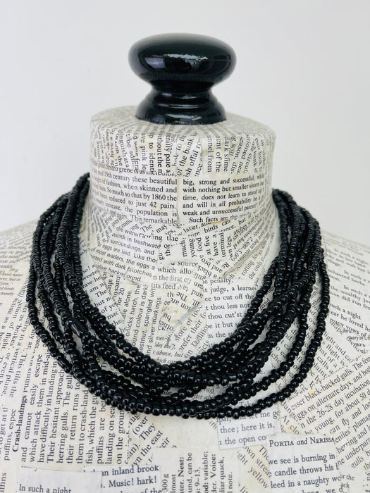 A black beaded necklace displayed on a book-print mannequin bust against a plain white background.