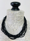 A black beaded necklace draped over a book-print mannequin bust against a plain white background.