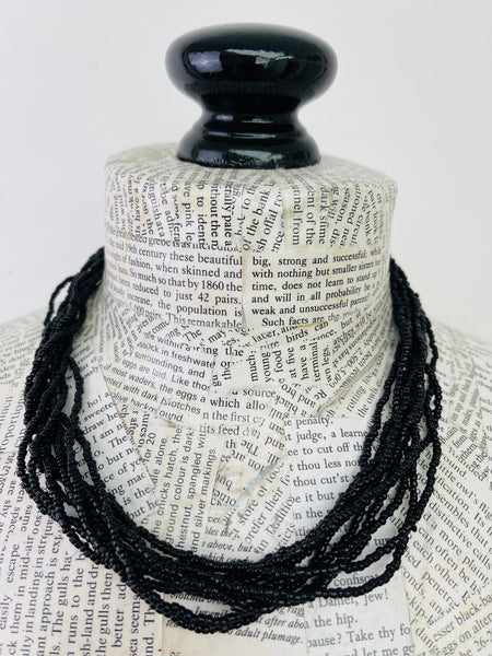 A black beaded necklace draped over a book-print mannequin bust against a plain white background.