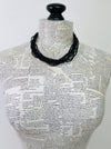 A black multi-strand beaded necklace displayed on a book-print mannequin torso against a plain white background.
