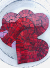 Cherry Red heart-shaped mosaic coasters with deep red hand-painted glass pieces on MDF base, photographed from above on a light textured surface.