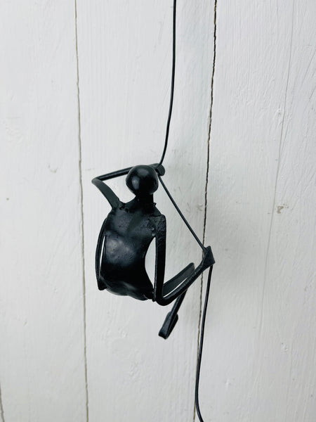 Black metal climbing man wall sculpture hanging by a flexible wire cord