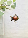 Lifestyle image of copper fish hook hanging on a wall near greenery.