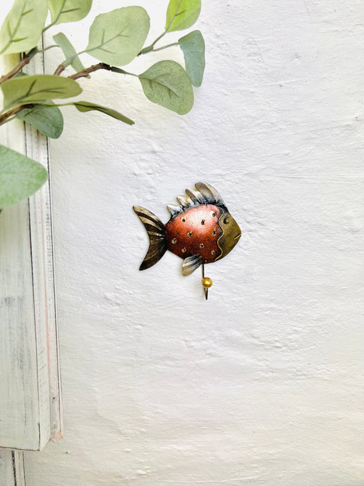 Lifestyle image of copper fish hook hanging on a wall near greenery.