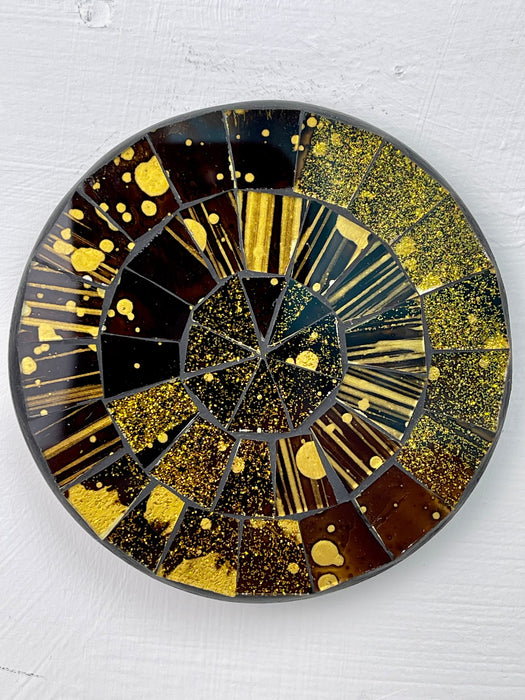 A round mosaic coaster with a firecracker design, primarily in shades of brown and gold, with black accents and a mix of geometric patterns and explosive shapes.